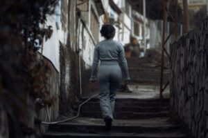 A woman in casual attire walks up concrete steps in a gritty urban environment, ideal for themes of solitude and determination.