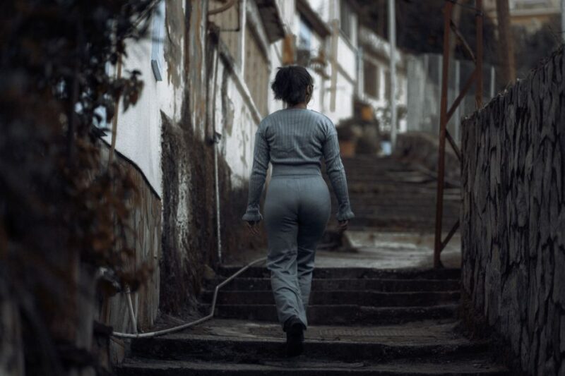 A woman in casual attire walks up concrete steps in a gritty urban environment, ideal for themes of solitude and determination.